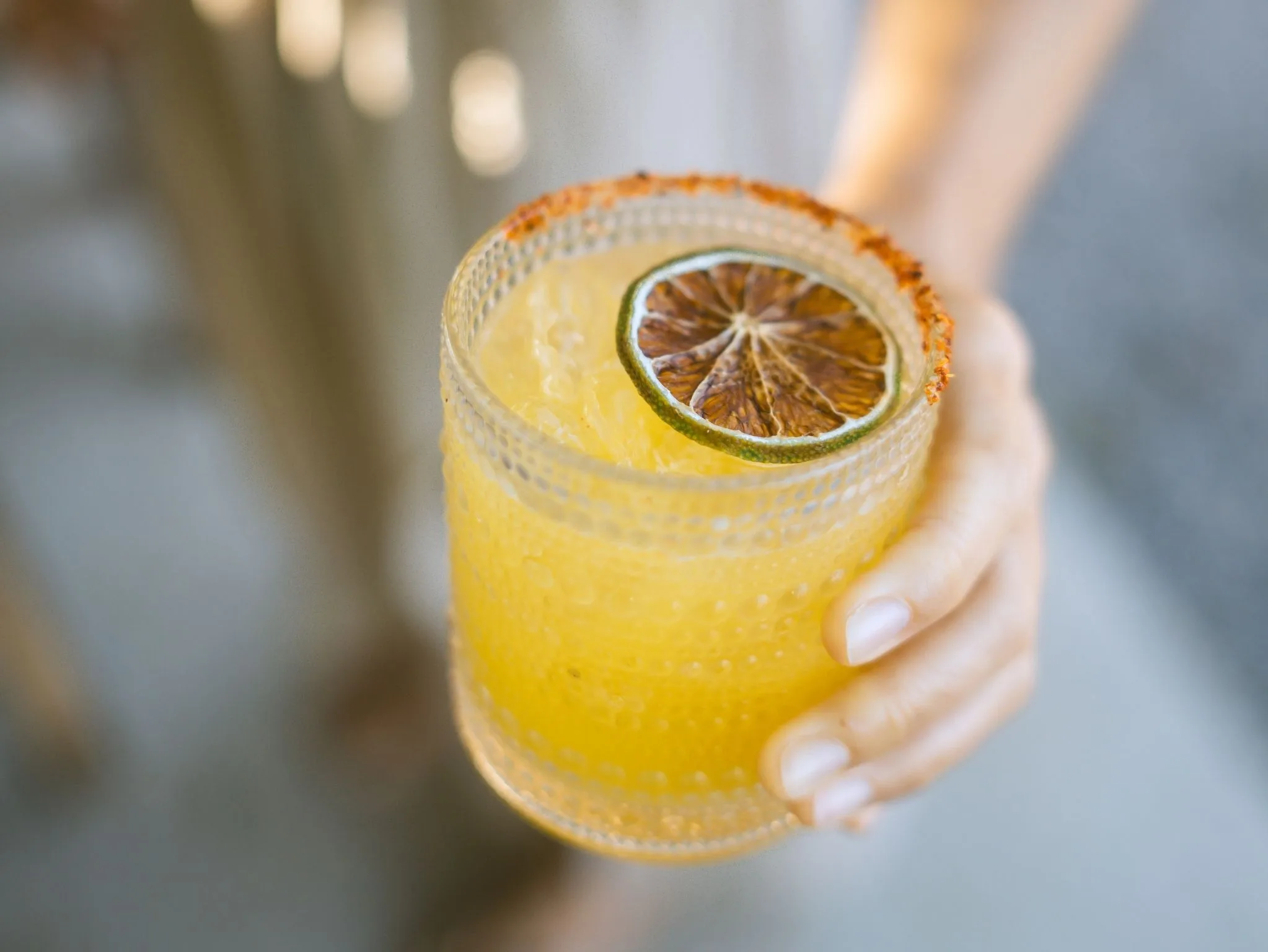 Cachasol Margarita with a dried lime wheel, held up in the afternoon light
